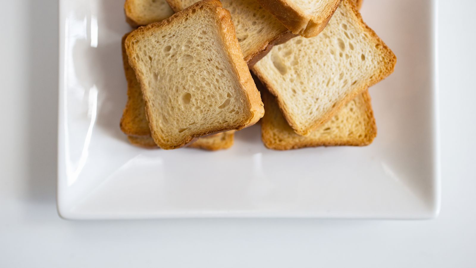 Golden toasted bread slices on a plate next to an air fryer basket