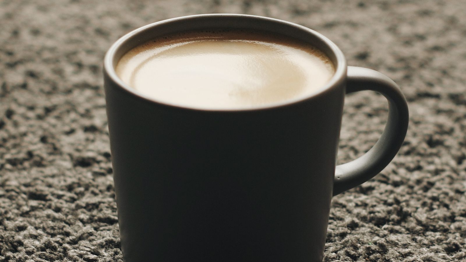 Coffee spilled on a light-colored carpet next to a cup