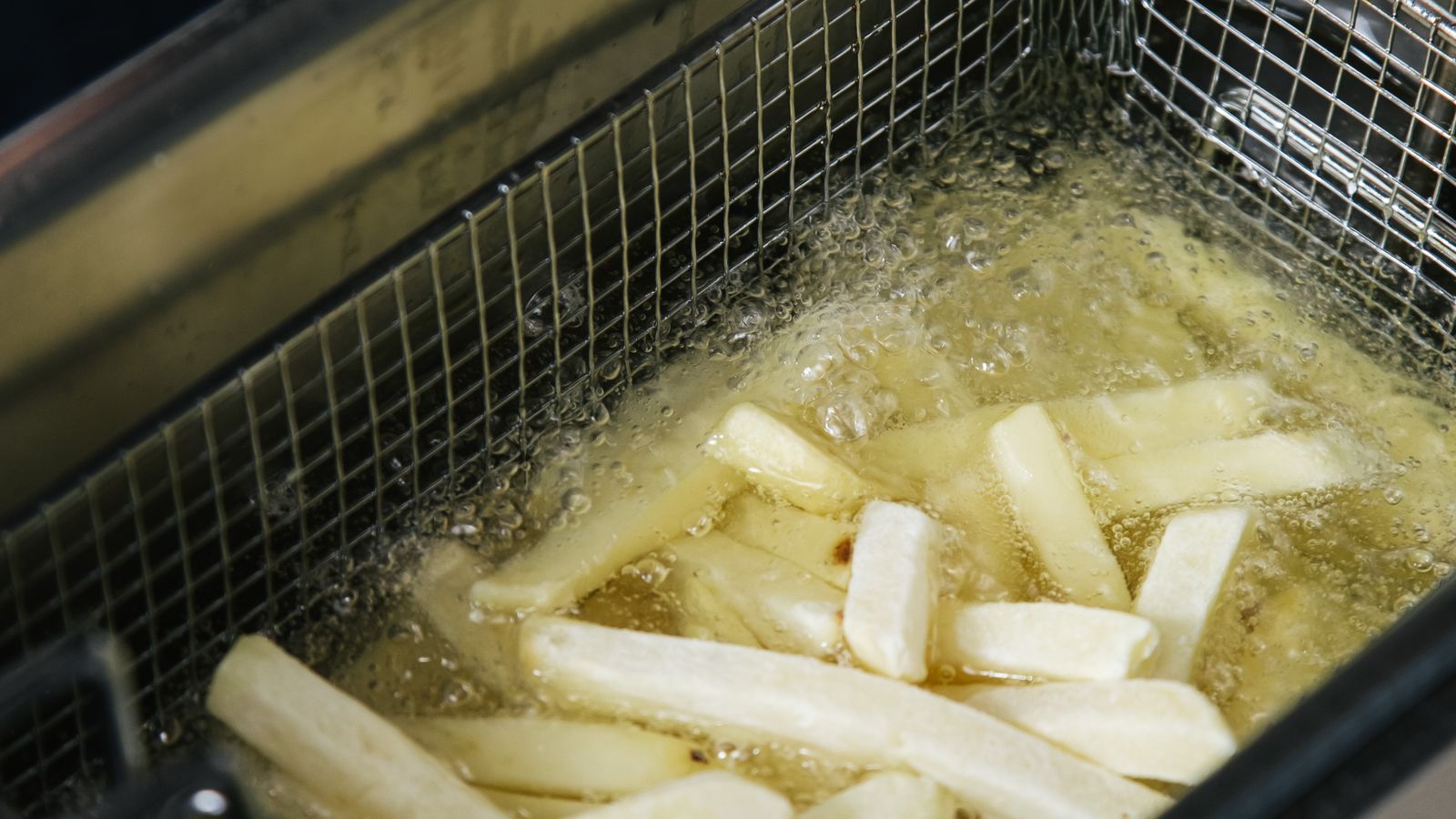 Golden fried food cooking in a perforated air fryer basket pan