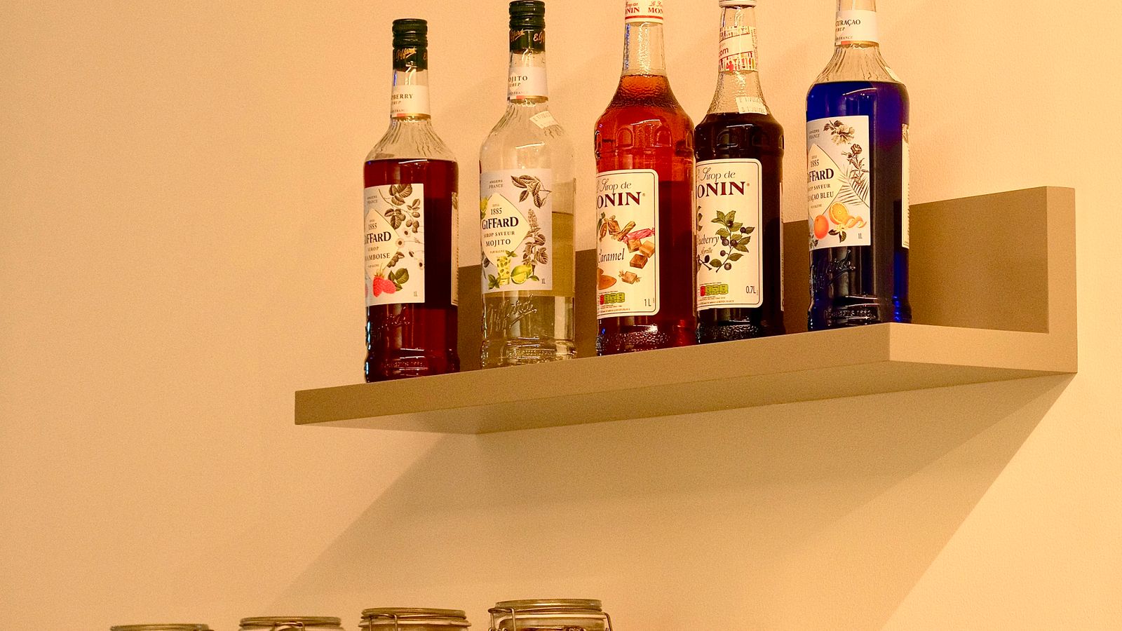 Wall-mounted kitchen shelf holding jars and cookware near a countertop