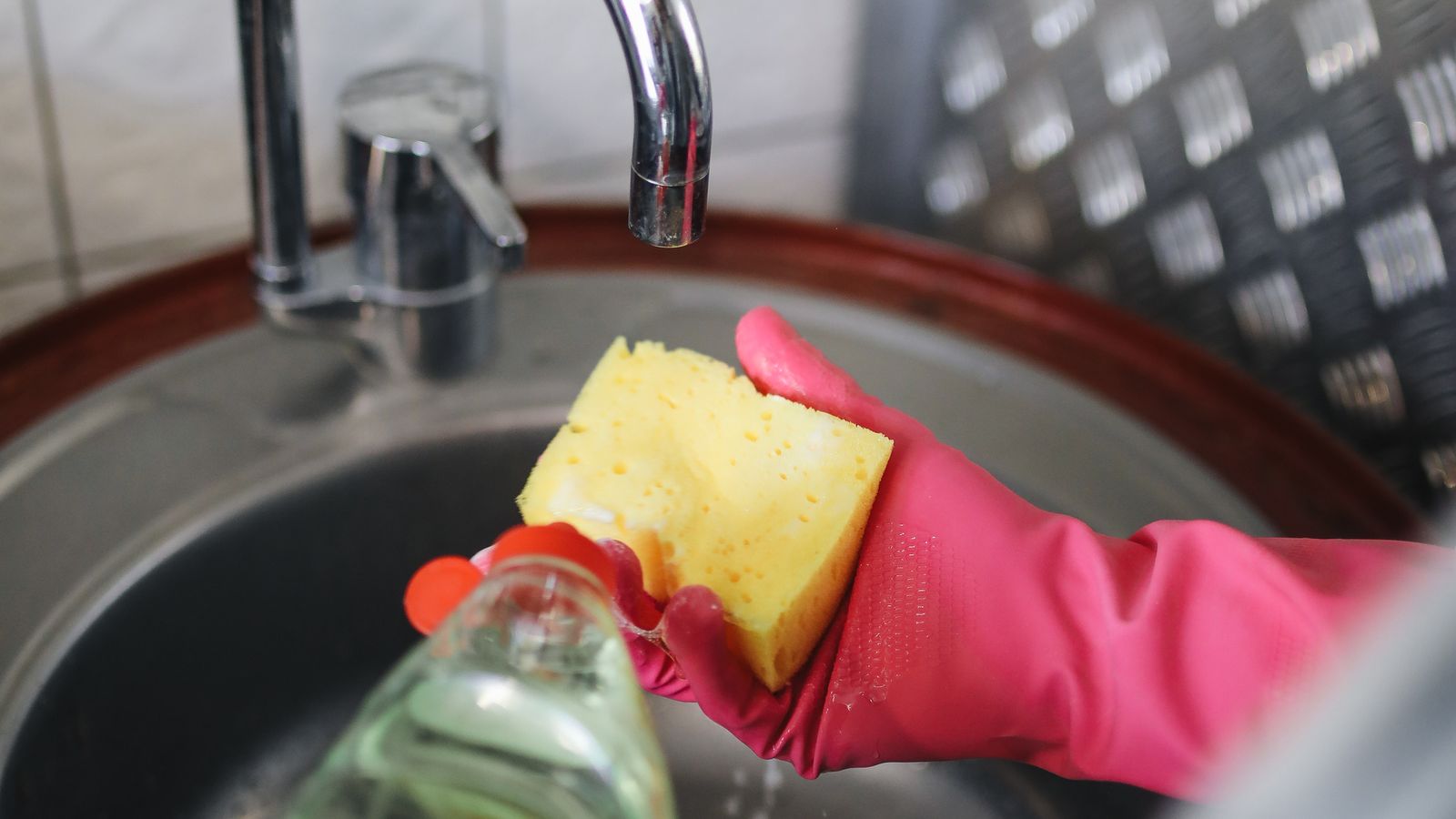 Kitchen cleaning supplies including sponge, gloves, and dish soap used for deep cleaning appliances