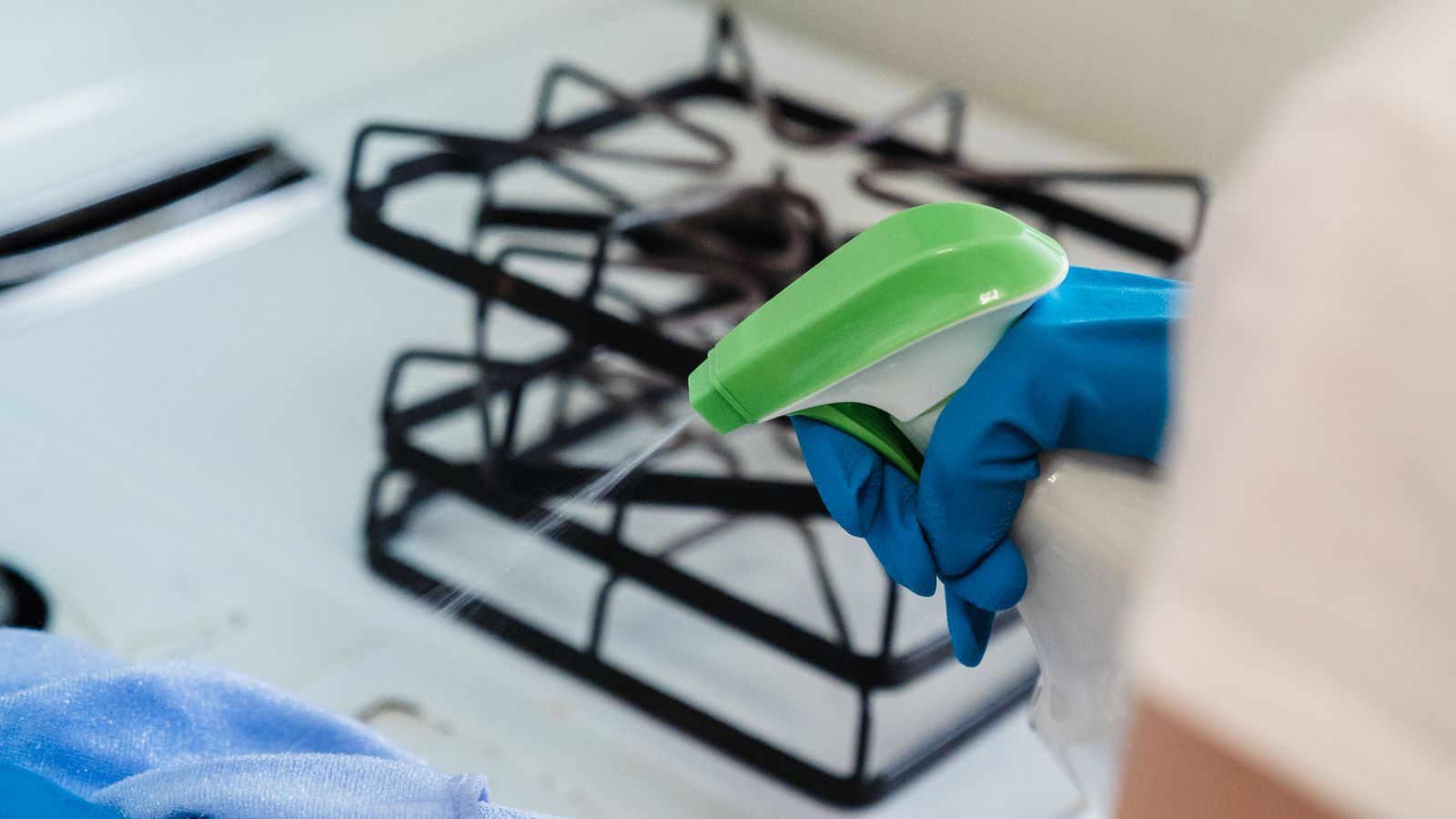 Person wearing gloves cleaning a kitchen appliance with a sponge and cleaning spray