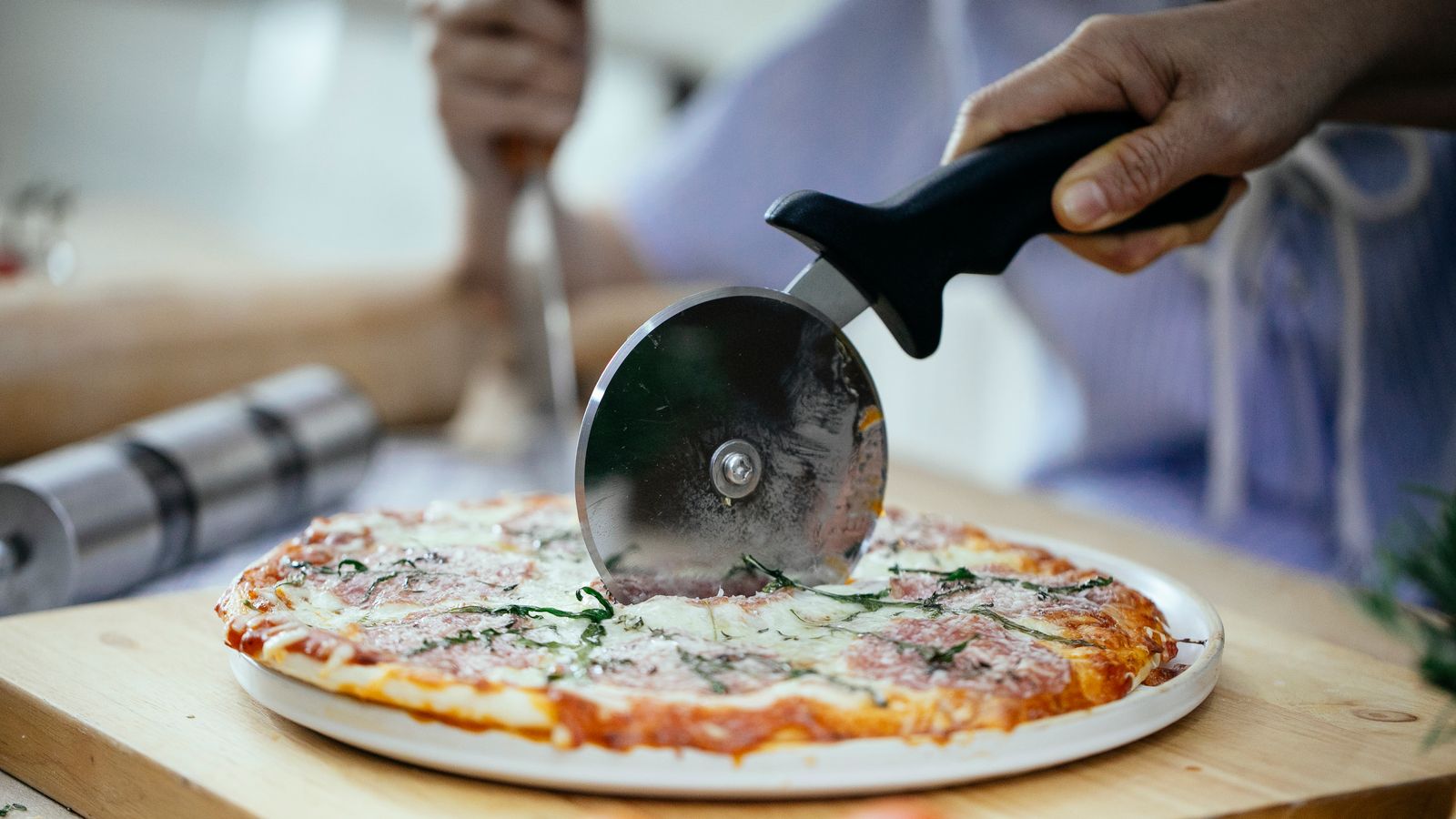 Rolling pizza cutter slicing through a freshly baked pizza crust on a wooden board