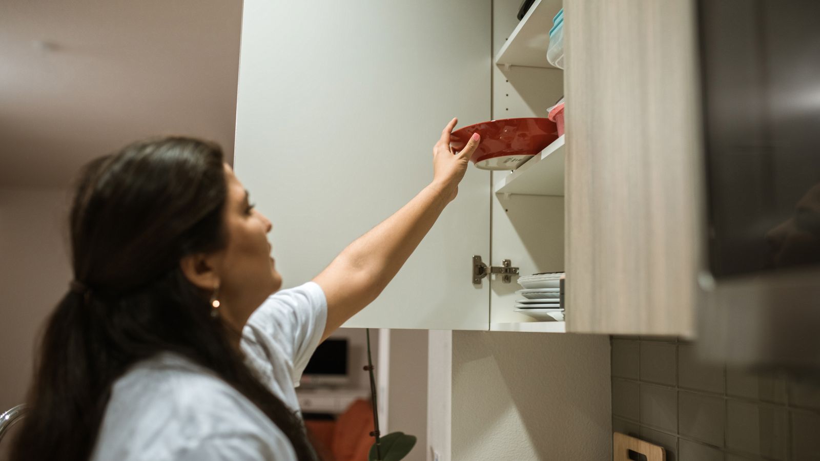 Woman organizing kitchen cabinet shelves with jars and cookware for a tidy air fryer prep station