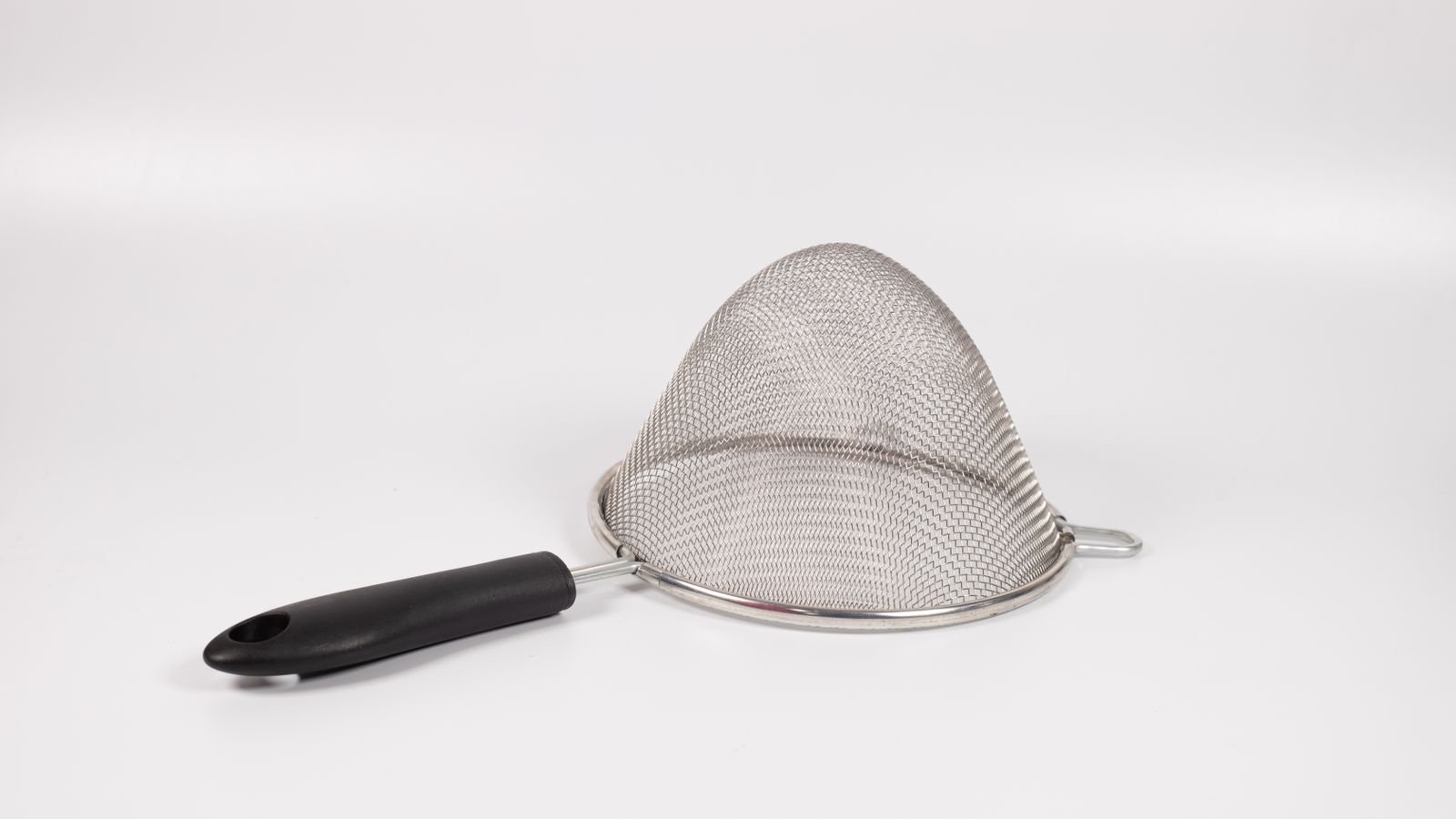 Stainless steel splatter screen with handle stored upright near kitchen prep tools