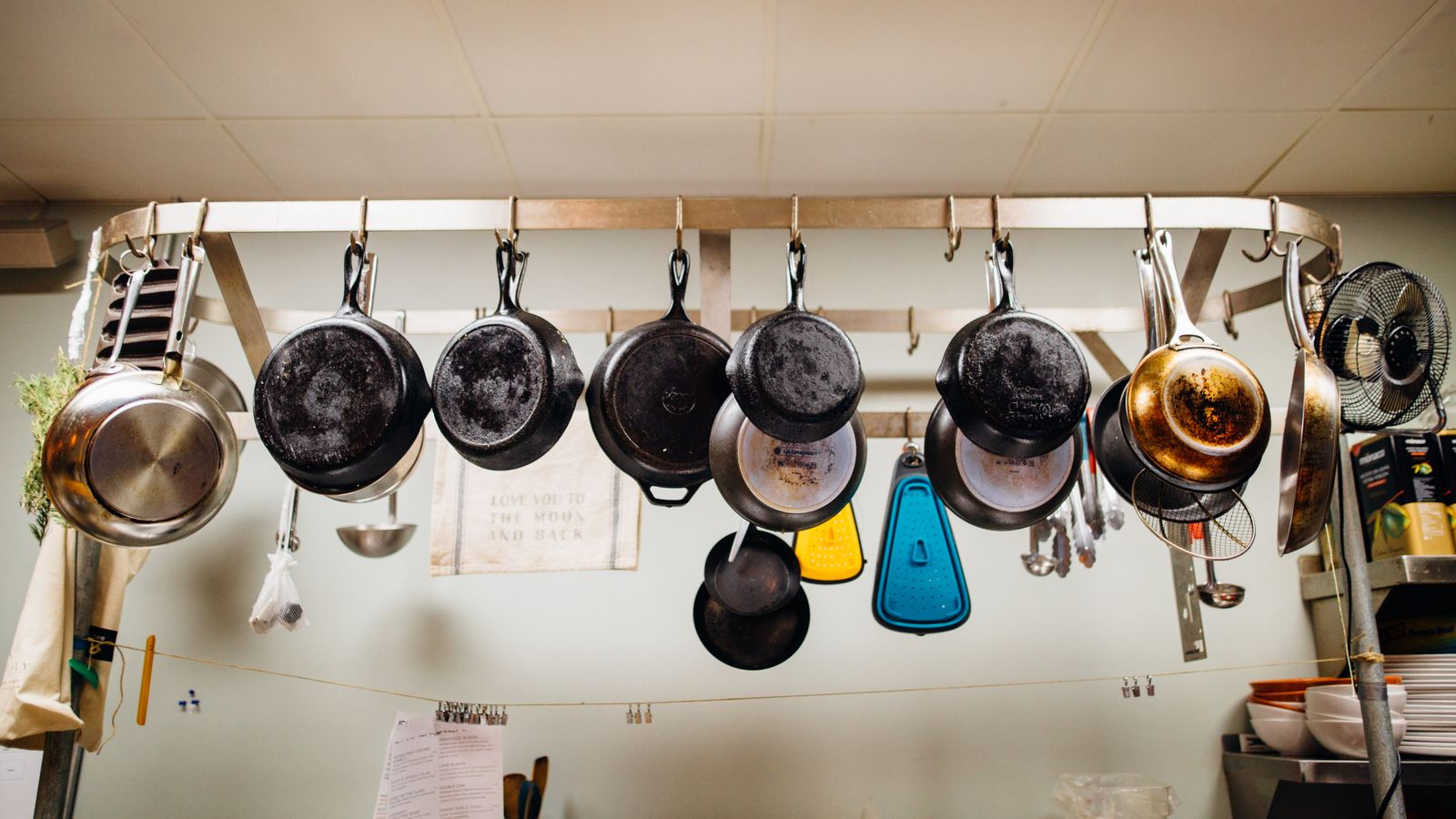 Assorted frying pans hanging in an organized row on a kitchen storage rack