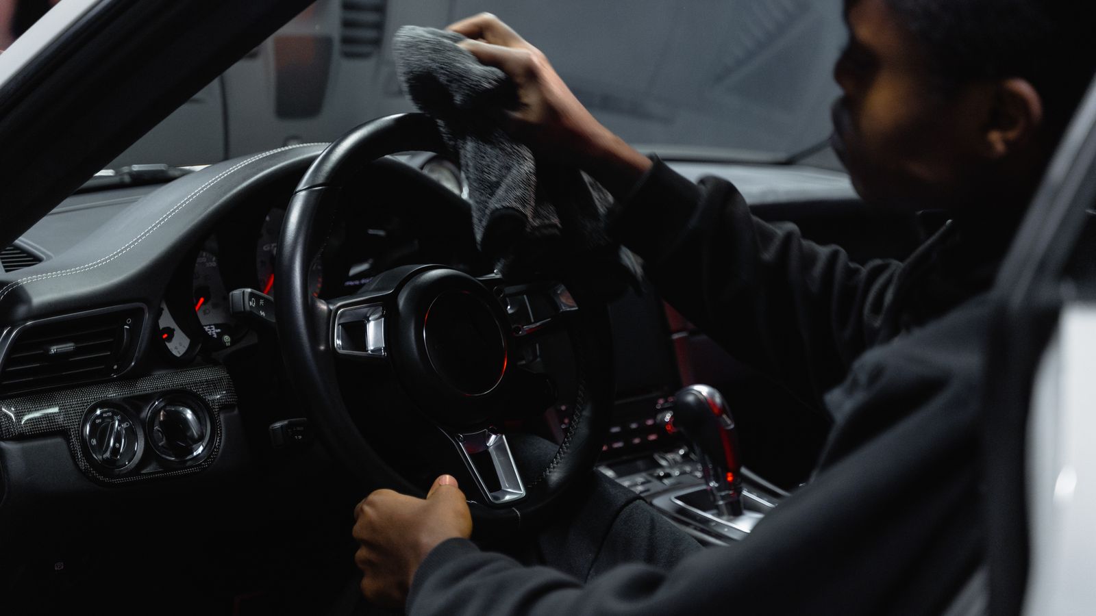 Person using a handheld carpet cleaner on a car's fabric seat and footwell