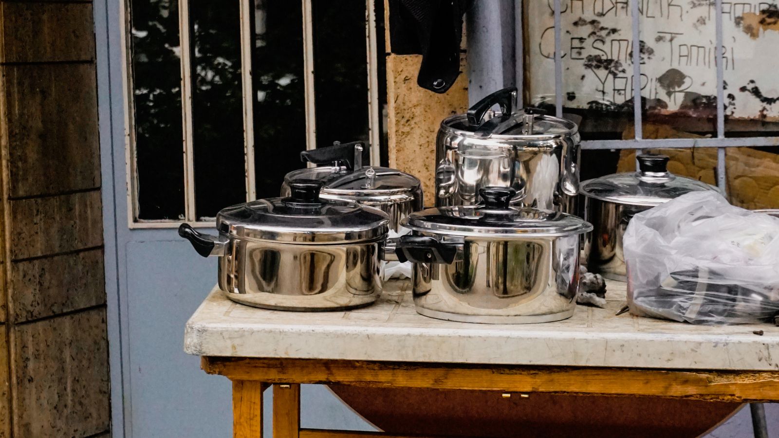 A budget cookware collection of stainless steel pots and pans arranged on a wooden kitchen table