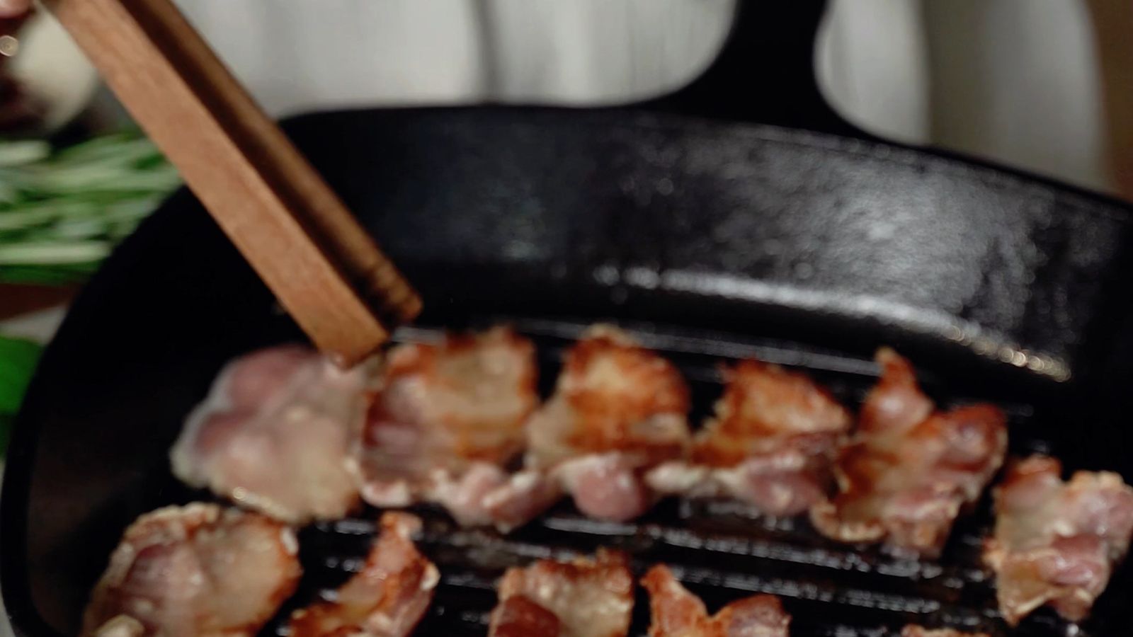 Bacon strips sizzling in a skillet, a scenario where a grease splatter guard helps keep the stovetop clean