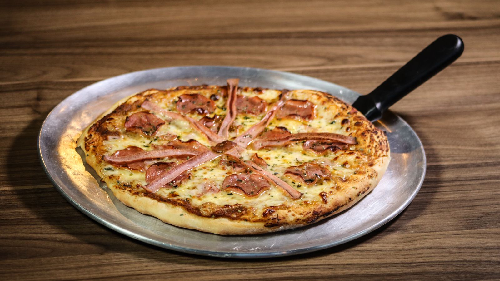 Overhead view of a pepperoni pizza on a metal tray ready for slicing