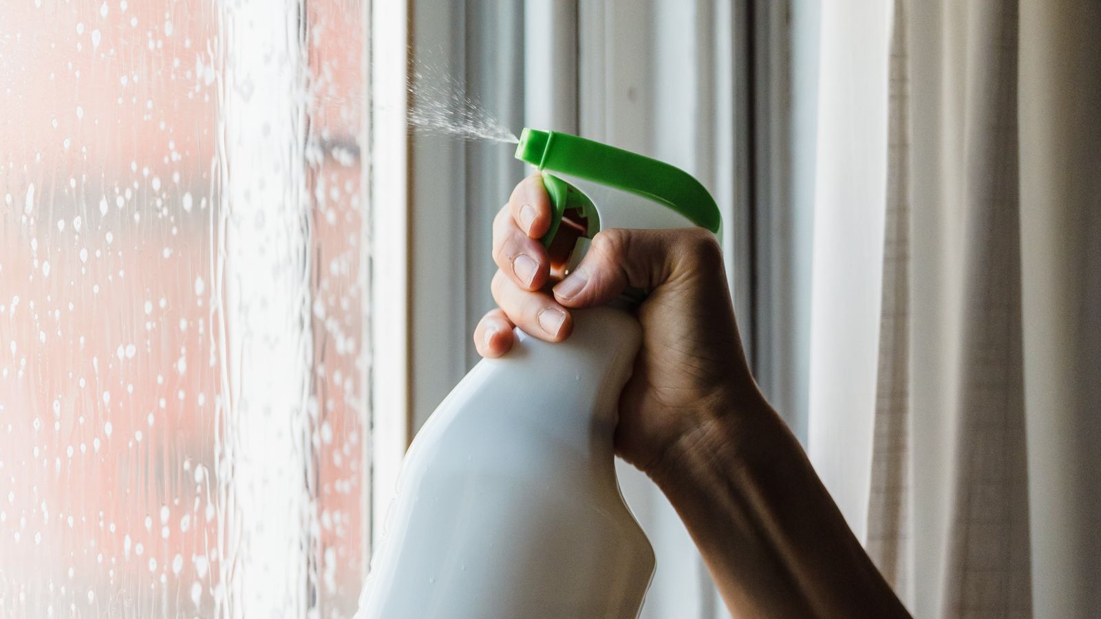 Hand using a spray bottle to apply cleaning solution to a glass surface