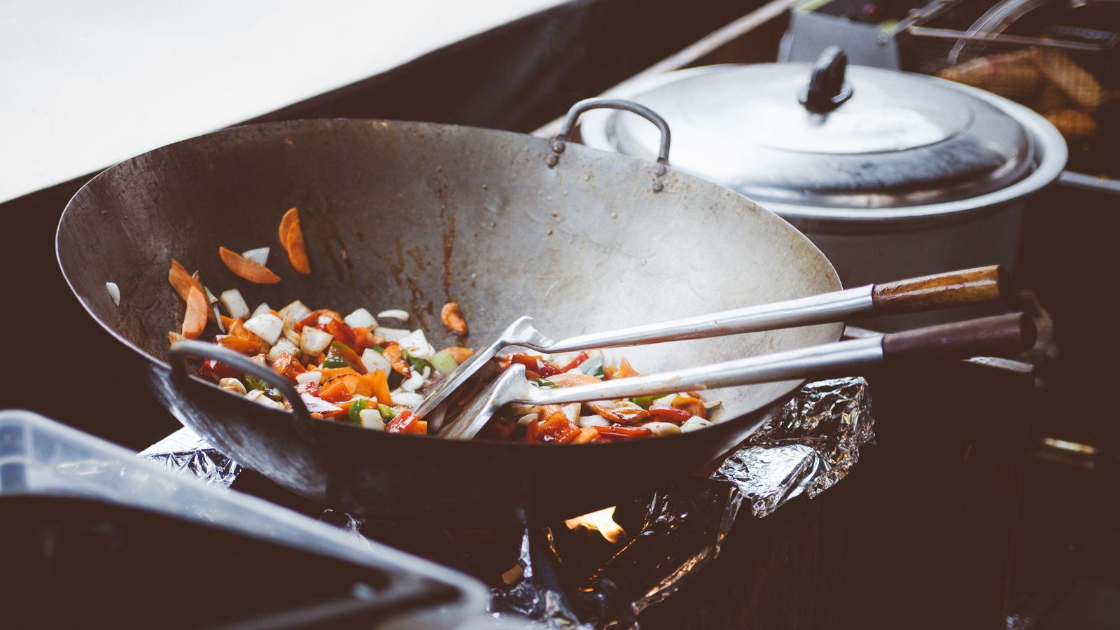 Chef tossing vegetables and noodles in a hot wok with rising flames
